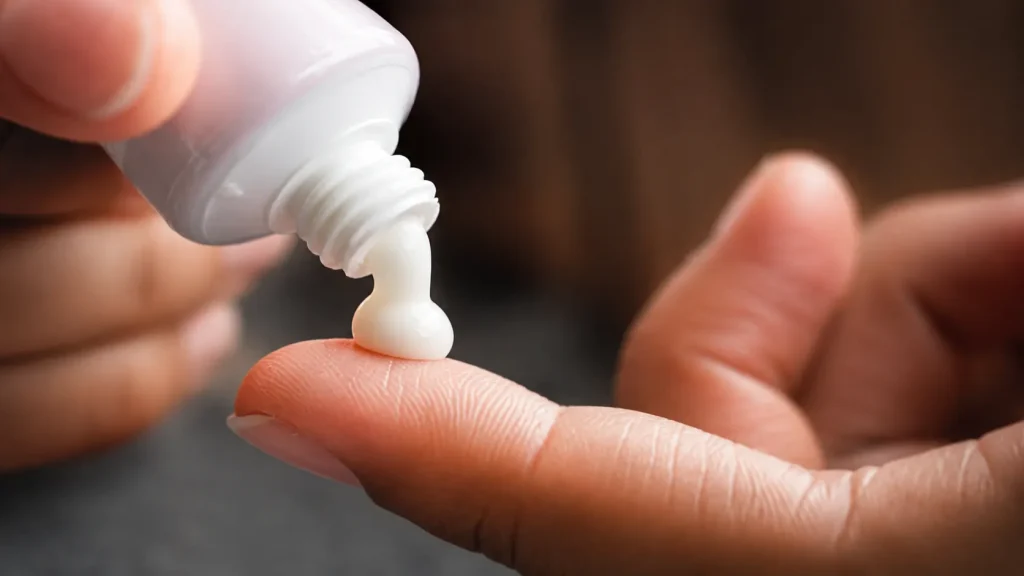 Close-up of a small rice-grain-sized amount of estradiol cream being dispensed onto a fingertip for safe facial application.