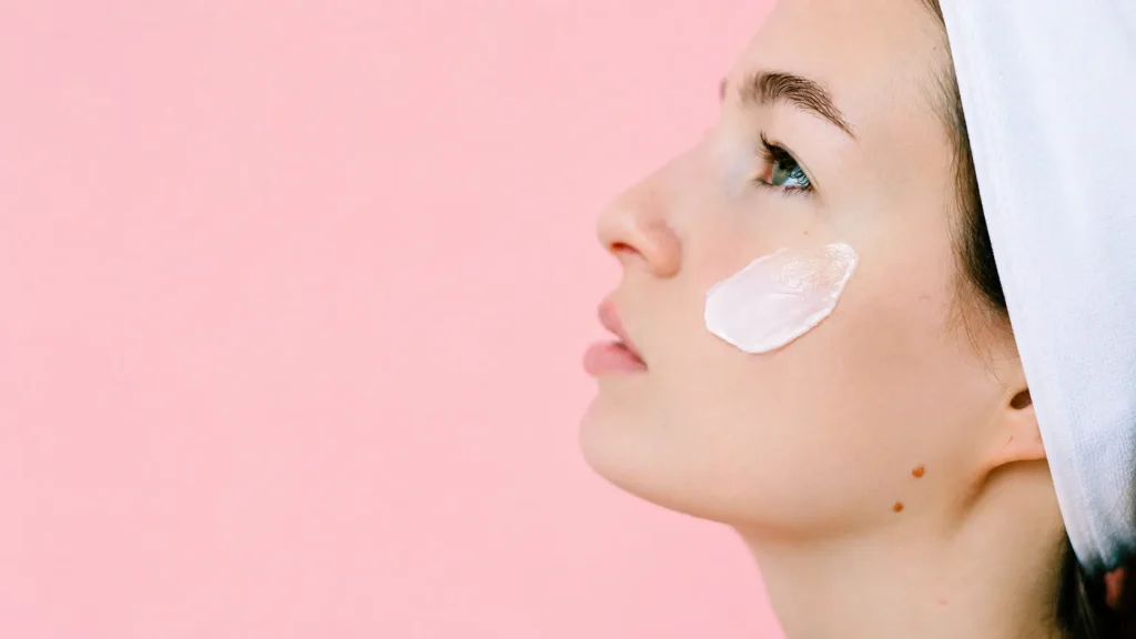 Woman applying facial moisturizer cream on clean skin during a natural skincare and beauty routine.