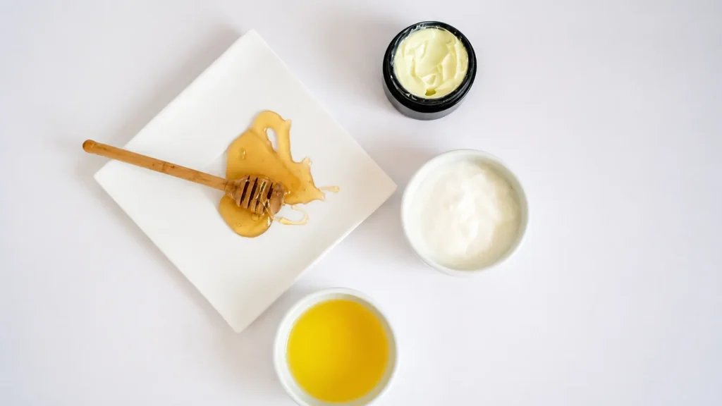 Homemade face cream with honey, natural oils, and moisturizing skincare ingredients arranged on a clean white background.