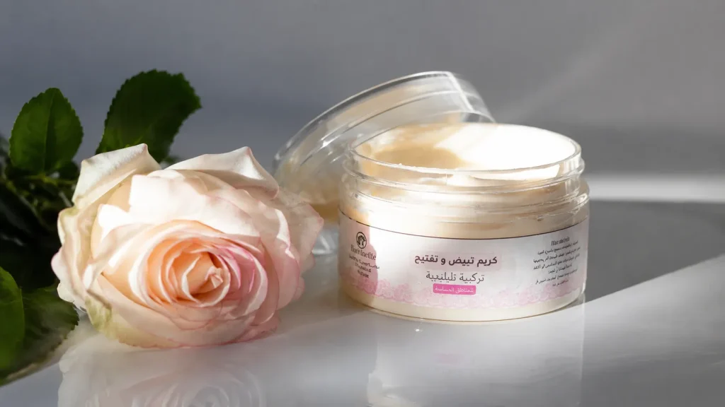 Natural face cream in an open cosmetic jar beside a soft pink rose, showcasing a moisturizing skincare product for healthy skin.