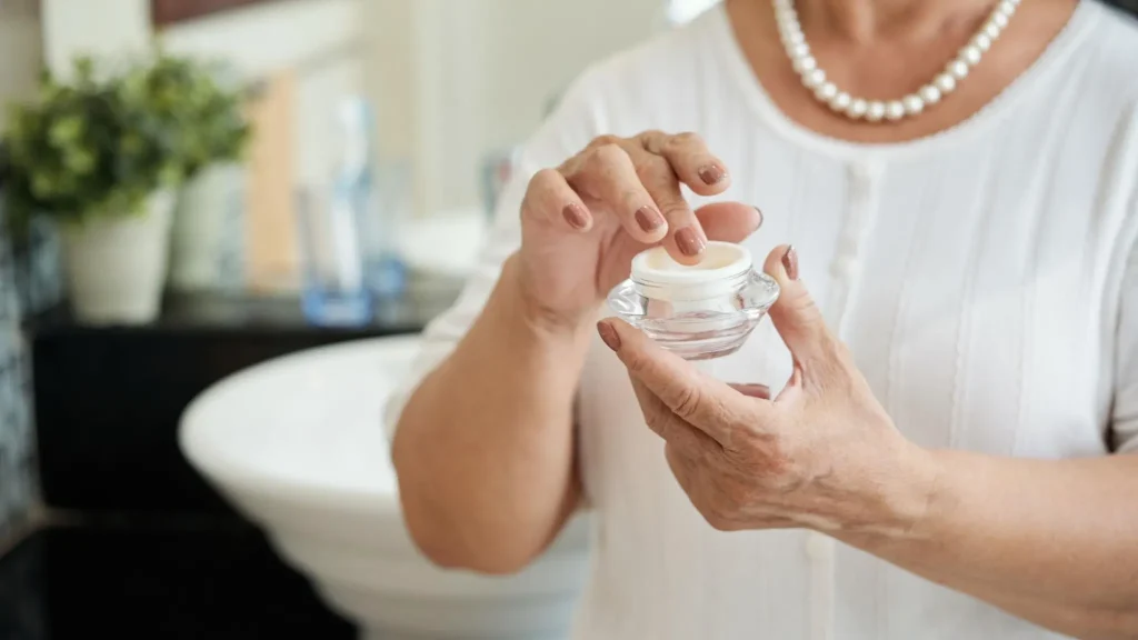 Woman applying cream on her face as part of an anti-aging skincare routine.
